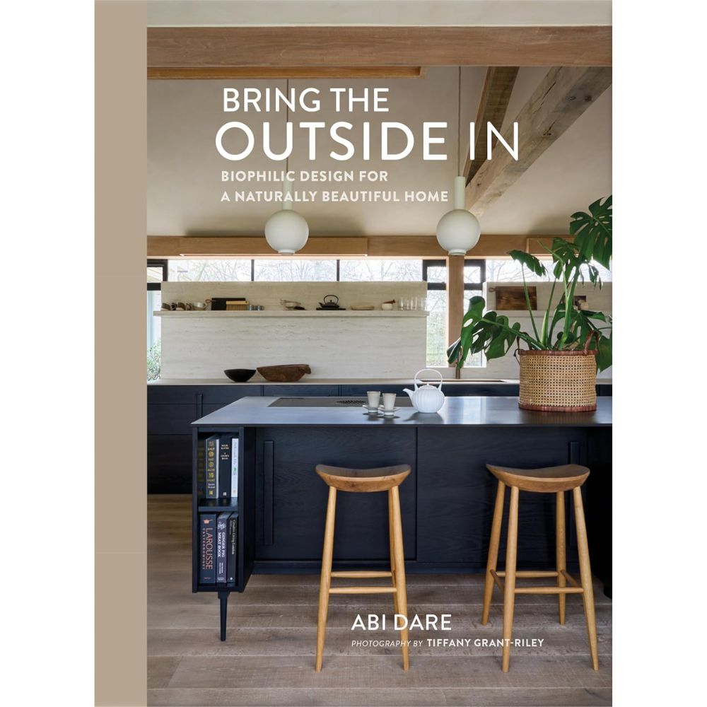 עטיפת הספר "Bring the Outside In" מאת Fine Lab Home, המציגה מטבח מודרני עם שרפרפים מעץ, אי שחור, חלונות גדולים וצמחים, המשקף עיצוב ביופילי וחיבור לטבע.