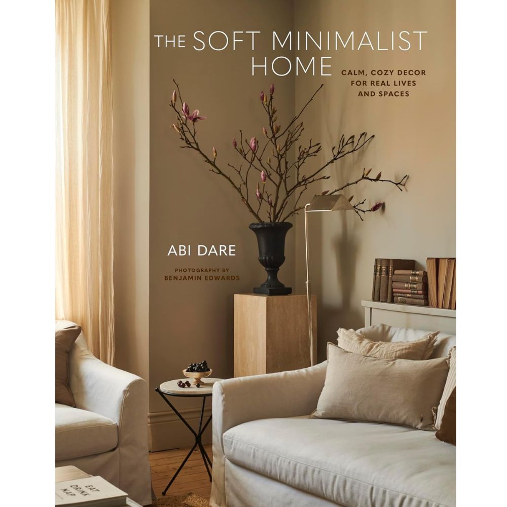 ספר העיצוב "The Soft Minimalist Home" מבית Fine Lab Home, עם כריכה המציגה סלון בגוונים טבעיים, ספות בהירות, אגרטל עם ענפים ועיצוב מינימליסטי רך.