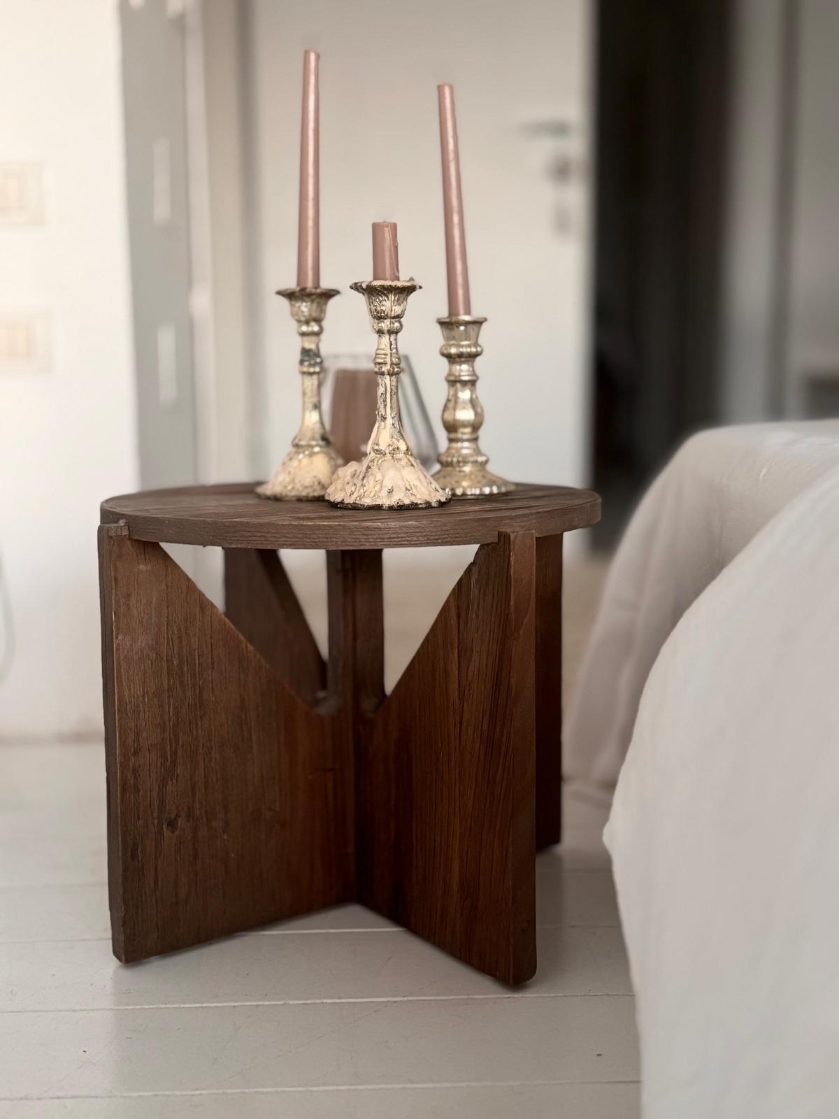 שולחן צד קטן ועגול, סטול נורדי עץ, מחזיק שלושה פמוטים מעוטרים עם נרות ורודים ליד המיטה, ומוסיף סגנון עיצוב נורדי עדין לחדר המואר באור רך.