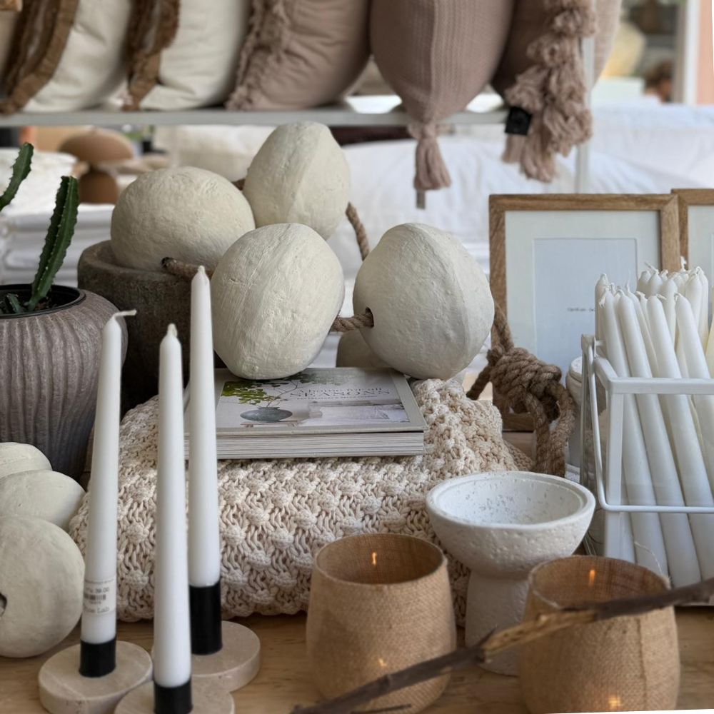 תצוגה לשולחן הכוללת זוג נרות בגוון לבן מבית Fine Lab Home, קישוטים מרקמים, קקטוס בעציץ, תמונות ממוסגרות, טקסטיל ארוג וכלי קרמיקה בגוונים ניטרליים.