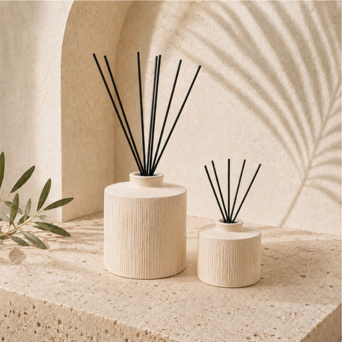 שני מפיצי ריח קרמיים בצבע בז' מבית Fine Lab Home — אחד גדול ואחד קטן, 'ORANGER מפיץ ריח קרמיקה' — מונחים על משטח אבן מרקם, עם צללי צמחים רכים וענף עלים סמוך, המדגישים את הקרמיקה בעבודת יד. כלי קיבול אלה ממלאים את האוויר בעדינות בניחוחות של פריחת הדרים, ומביאים אלגנטיות טבעית לכל חלל.