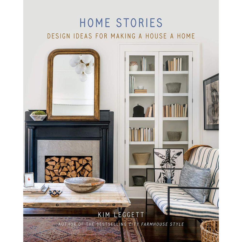 עטיפת הספר "Home Stories" בהוצאת Fine Lab Home: סצנה נעימה בסלון הכוללת אח, ערימת עצי הסקה, מראה, מדף ספרים, ספה ושולחן קפה.