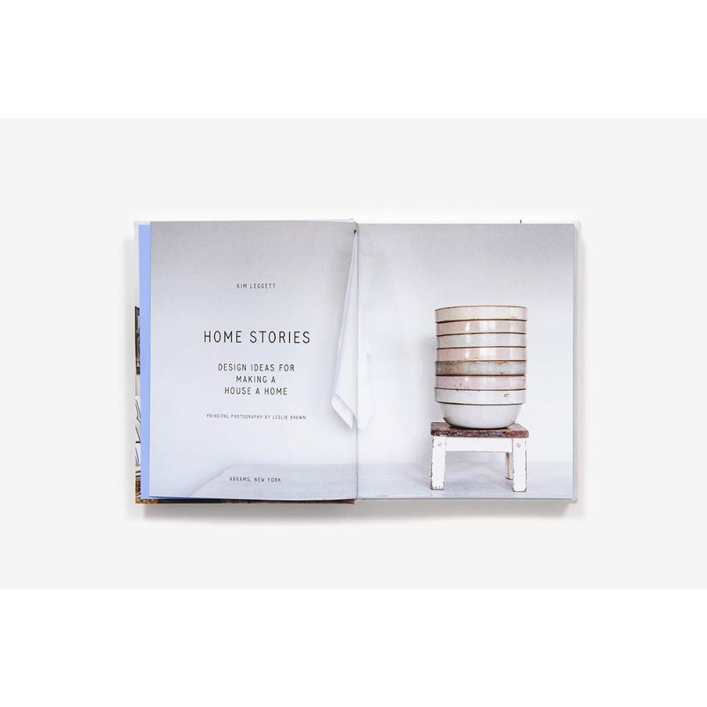 בספר העיצוב הפתוח "Home Stories" מבית Fine Lab Home, מוצג עמוד השער משמאל וקערות המונחות זו על גבי זו על שרפרף מימין, ומציע השראה לעיצוב הבית.
