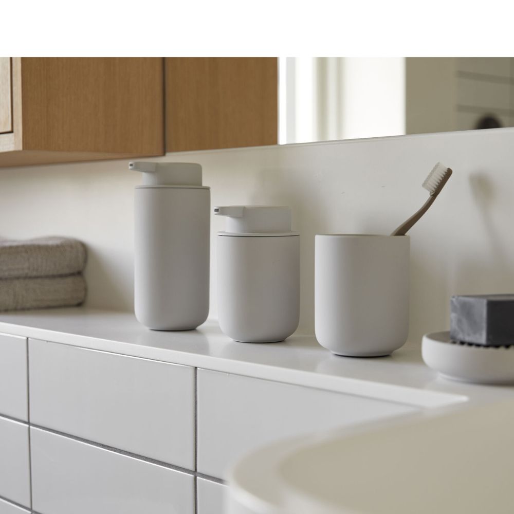 שלושה אביזרי אמבטיה של Fine Lab Home בצבע אפור מט — מתקן לסבון, מיכל עם מכסה וכוס למברשת שיניים בצבע אפור בהיר — מונחים על משטח לבן לצד מגבות מקופלות, ומוסיפים אלגנטיות בסגנון סקנדינבי לחדר שלכם.